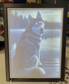 The same dog portrait lithophane illuminated, revealing the dog beside a lake